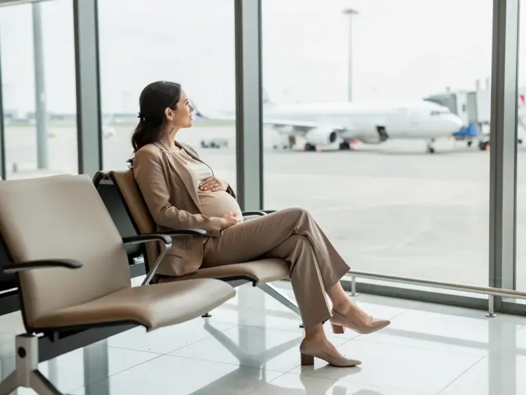 Schwangere Frau mit Reisetasche am Flughafen berufliche Reisen sicher planen